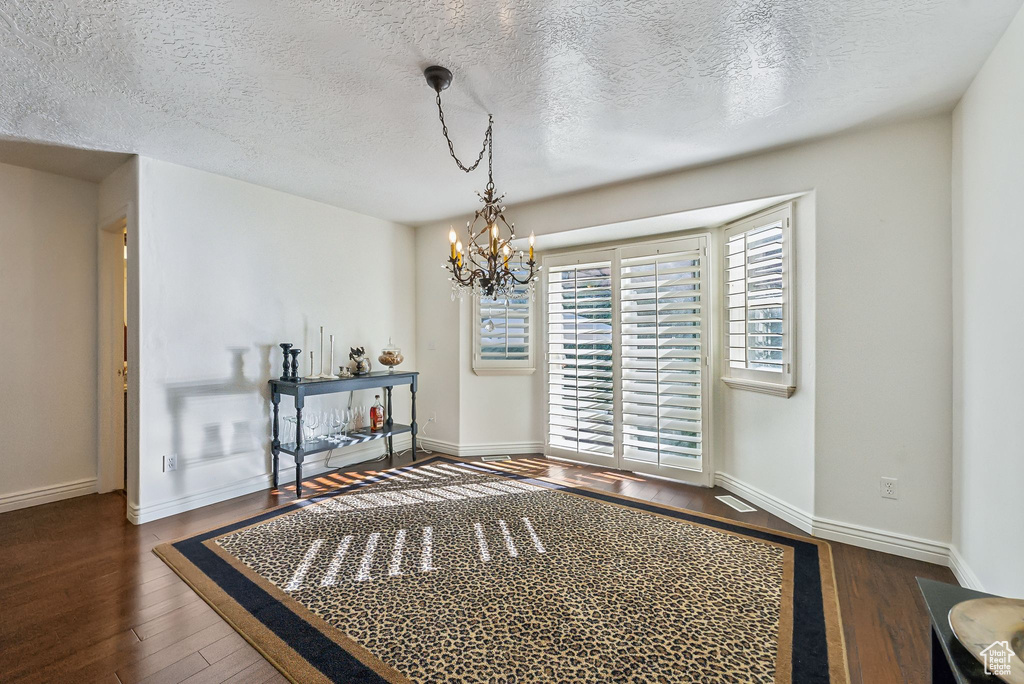 Interior space with a notable chandelier, dark wood-type flooring, and a textured ceiling