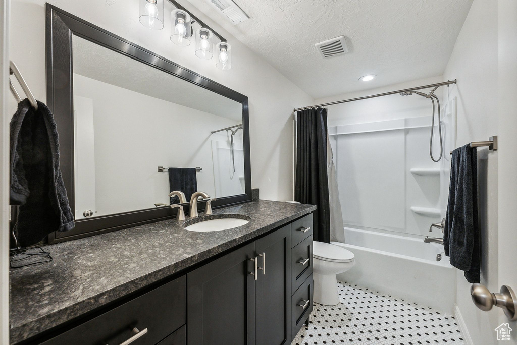 Full bathroom featuring shower / bath combination with curtain, a textured ceiling, vanity, and toilet