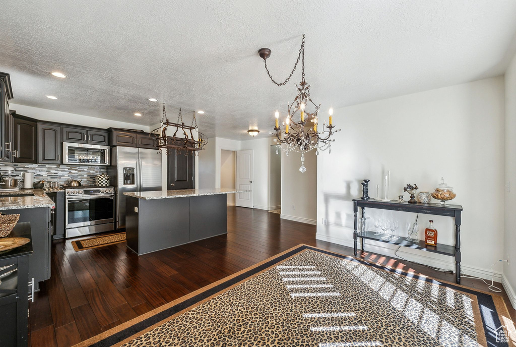 Kitchen with light stone counters, a kitchen island, dark brown cabinets, dark wood-type flooring, and stainless steel appliances