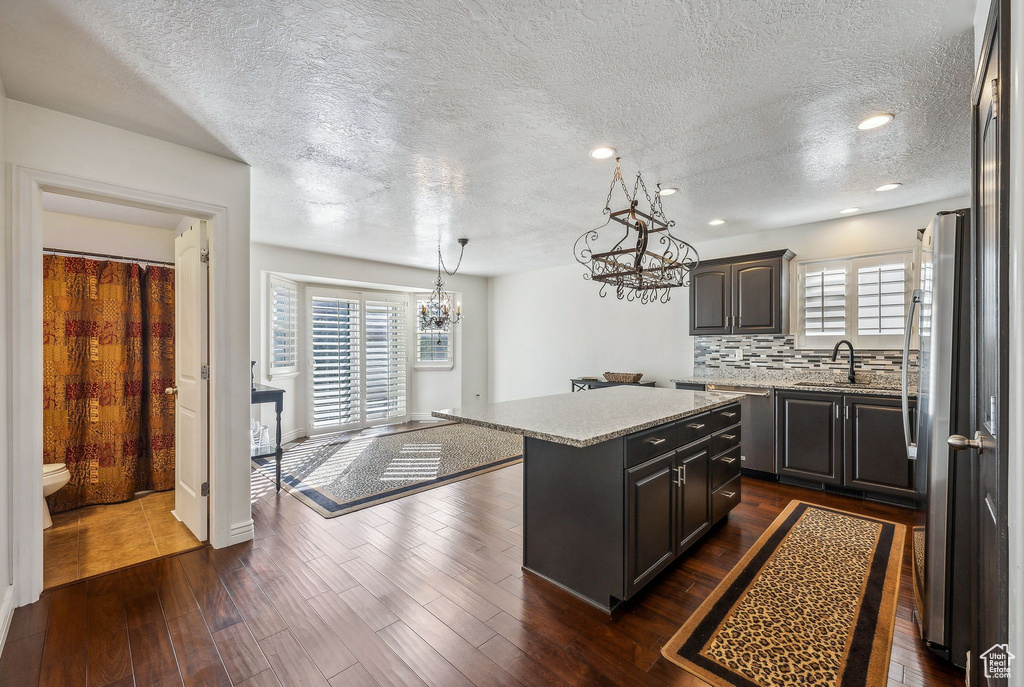 Kitchen with tasteful backsplash, a textured ceiling, a center island, an inviting chandelier, and dark hardwood / wood-style flooring