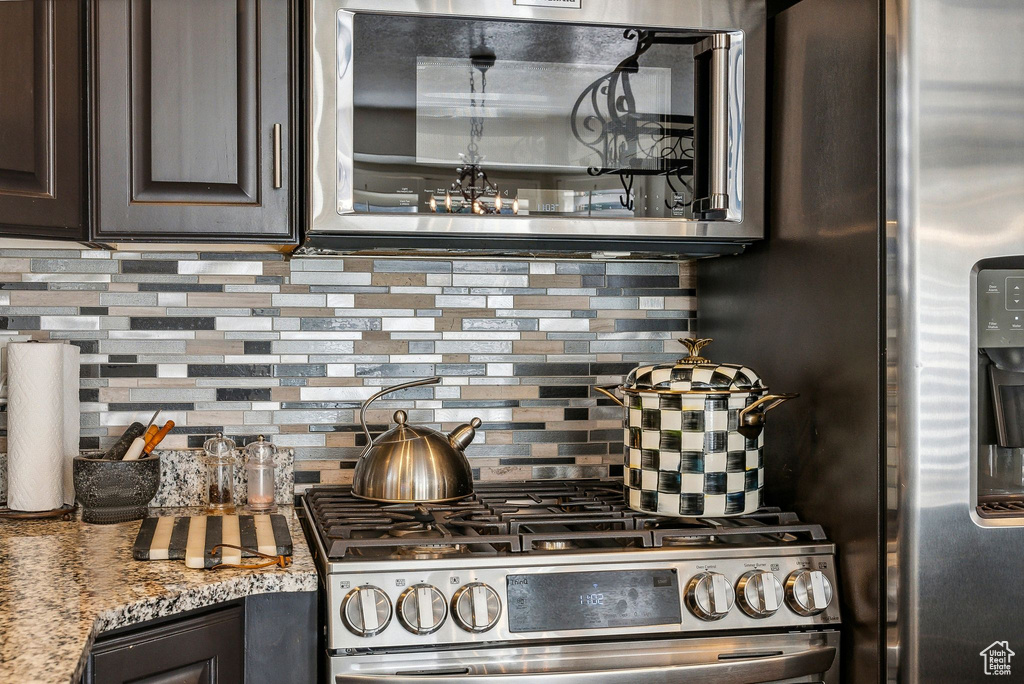 Kitchen featuring dark brown cabinets, light stone countertops, appliances with stainless steel finishes, and decorative backsplash