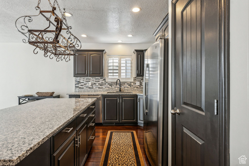 Kitchen with a textured ceiling, tasteful backsplash, dark wood-type flooring, sink, and stainless steel appliances