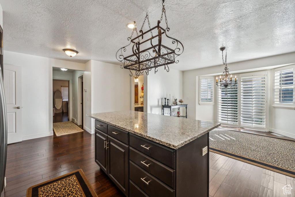 Kitchen with pendant lighting, a textured ceiling, a center island, dark hardwood / wood-style flooring, and light stone countertops