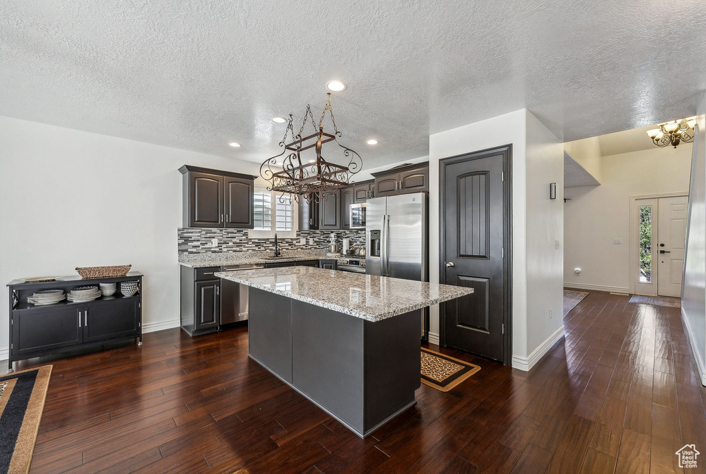 Kitchen featuring a textured ceiling, stainless steel appliances, dark wood-type flooring, and a kitchen island