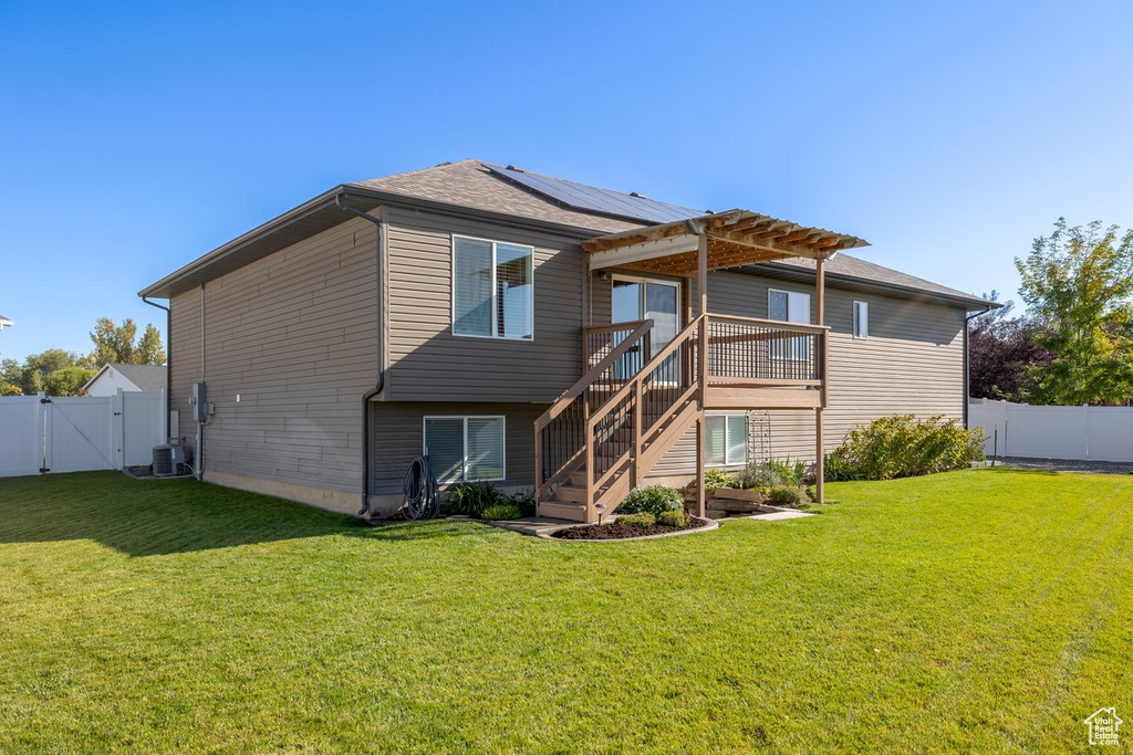 Back of house with a lawn, a deck, and central AC