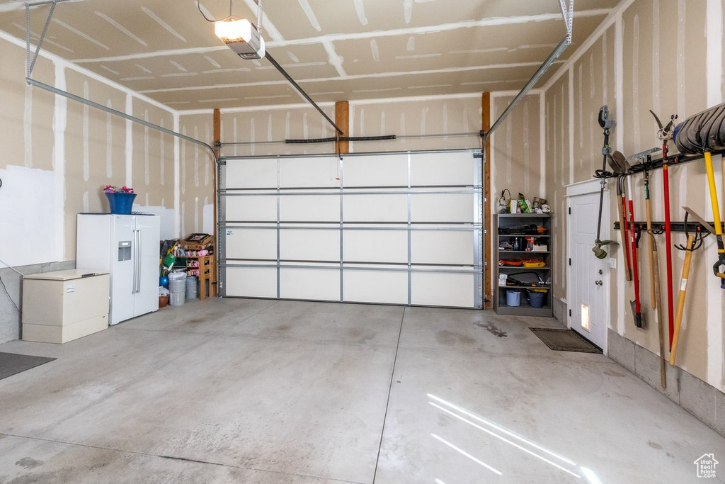 Garage featuring a garage door opener and white fridge with ice dispenser