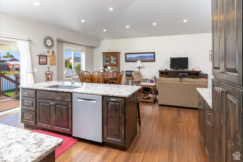 Kitchen featuring dark brown cabinetry, an island with sink, sink, stainless steel dishwasher, and dark wood-type flooring