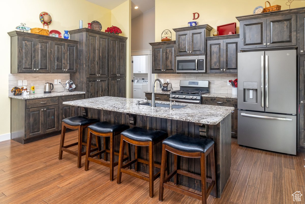 Kitchen featuring dark brown cabinets, a kitchen island with sink, stainless steel appliances, and dark wood-type flooring