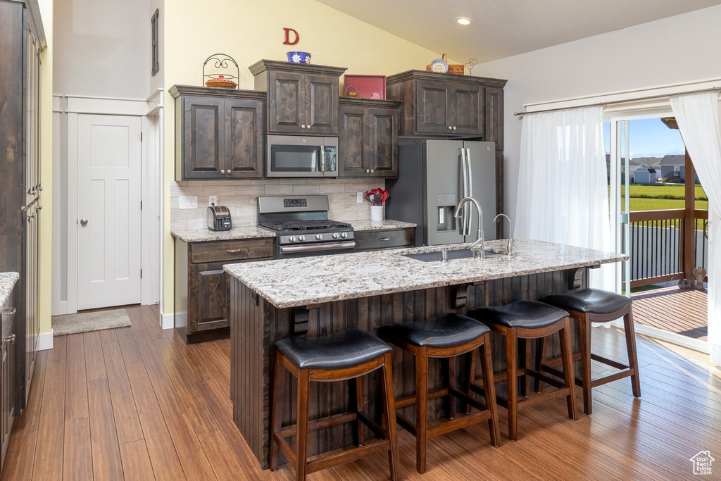 Kitchen featuring dark brown cabinets, a kitchen island with sink, vaulted ceiling, stainless steel appliances, and backsplash