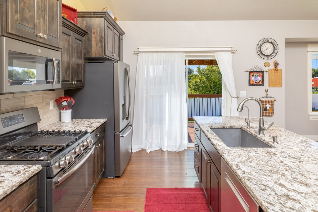 Kitchen featuring hardwood / wood-style flooring, sink, decorative backsplash, appliances with stainless steel finishes, and light stone countertops