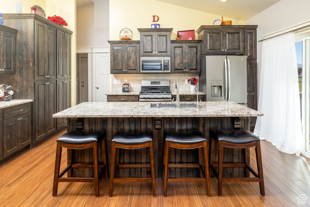 Kitchen featuring vaulted ceiling, a center island with sink, and appliances with stainless steel finishes