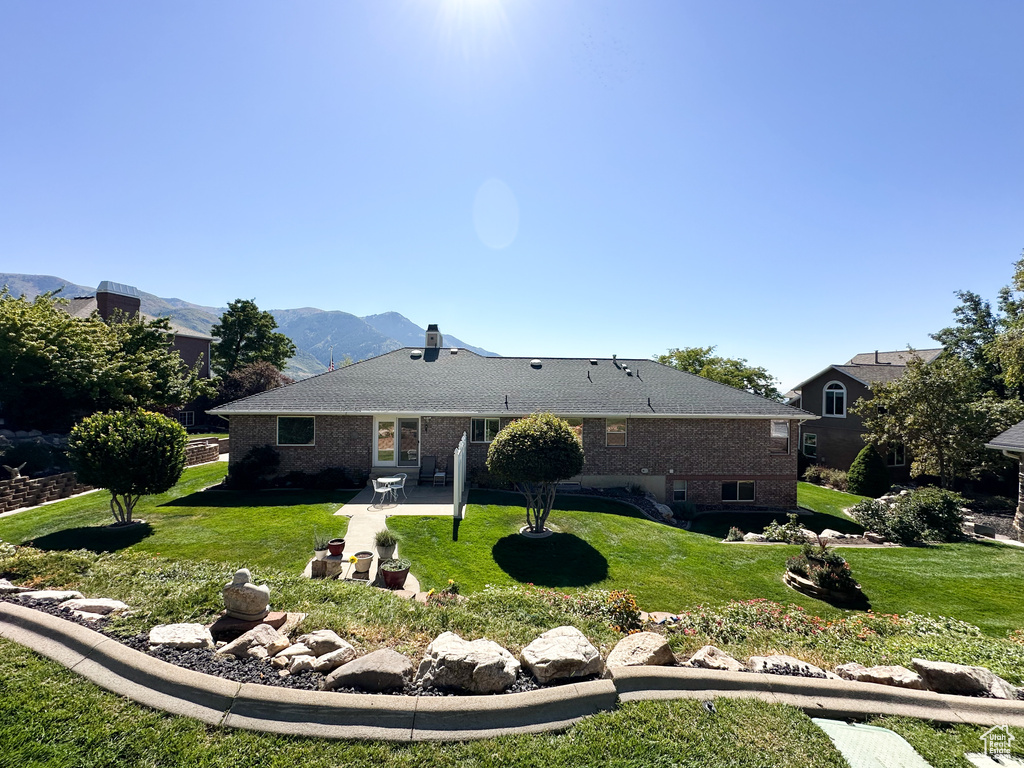 Rear view of house with a mountain view, a lawn, and a patio