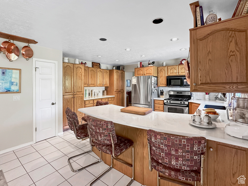 Kitchen featuring appliances with stainless steel finishes, decorative backsplash, light tile patterned flooring, a kitchen bar, and sink