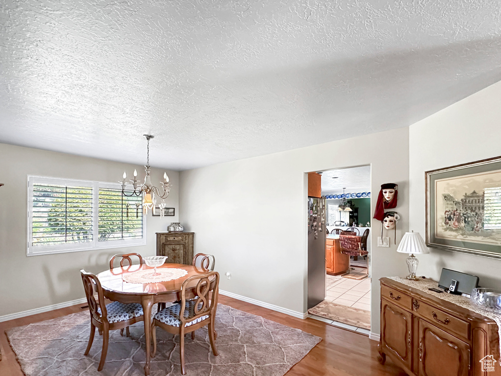 Dining space with a notable chandelier, light wood-type flooring, and a textured ceiling