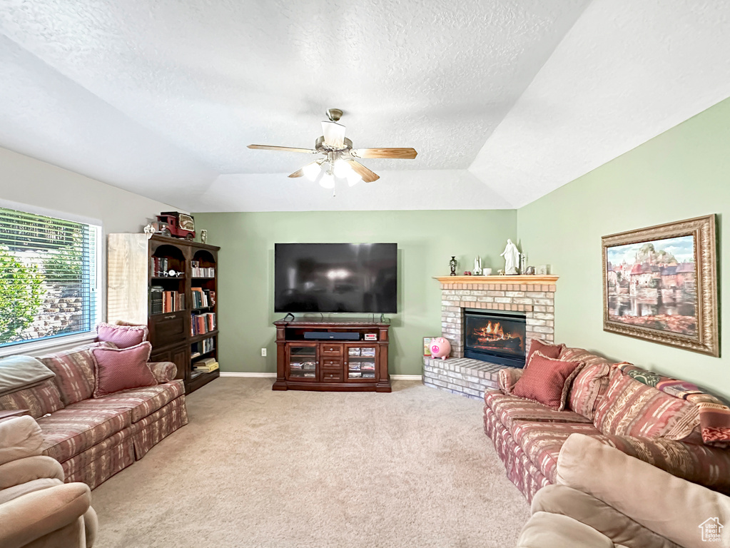 Carpeted living room with a fireplace, a textured ceiling, lofted ceiling, a tray ceiling, and ceiling fan