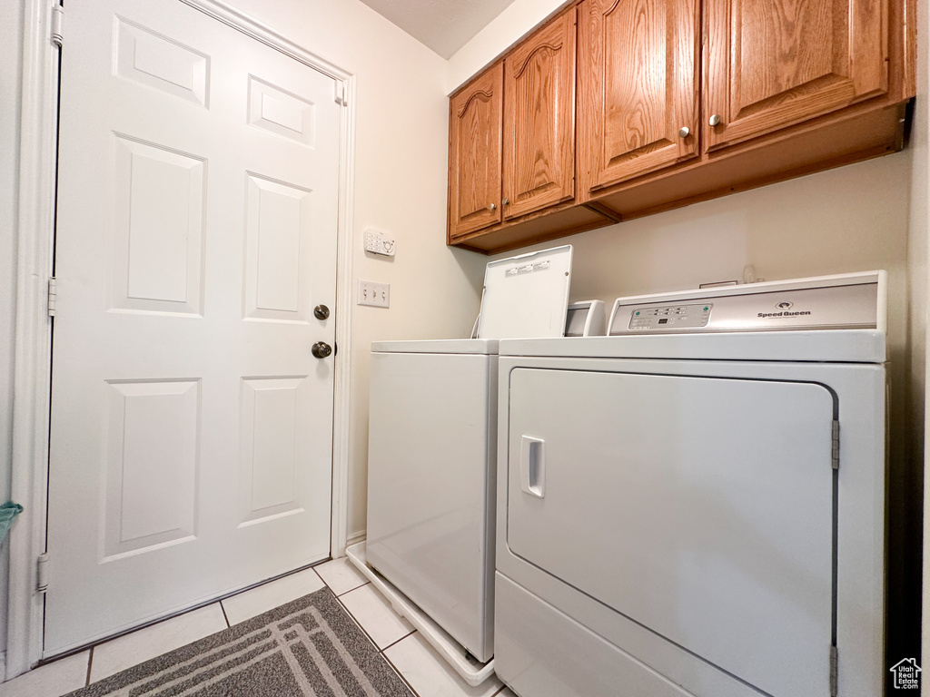 Laundry room featuring washing machine and dryer, light tile patterned floors, and cabinets