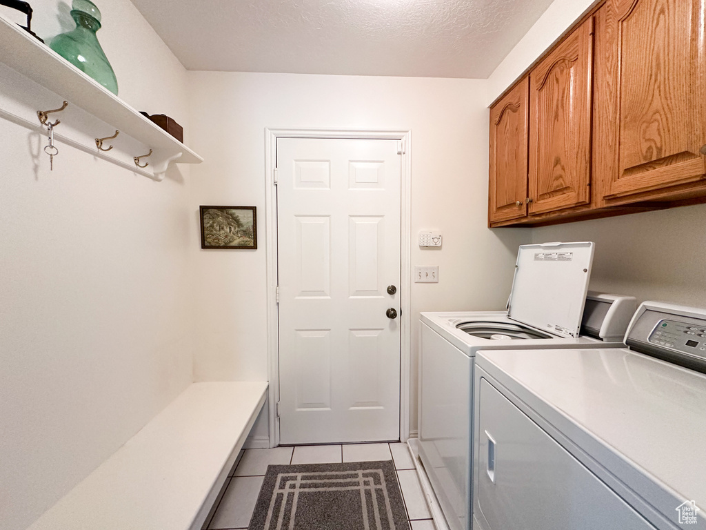 Laundry area featuring a textured ceiling, washer and clothes dryer, light tile patterned floors, and cabinets