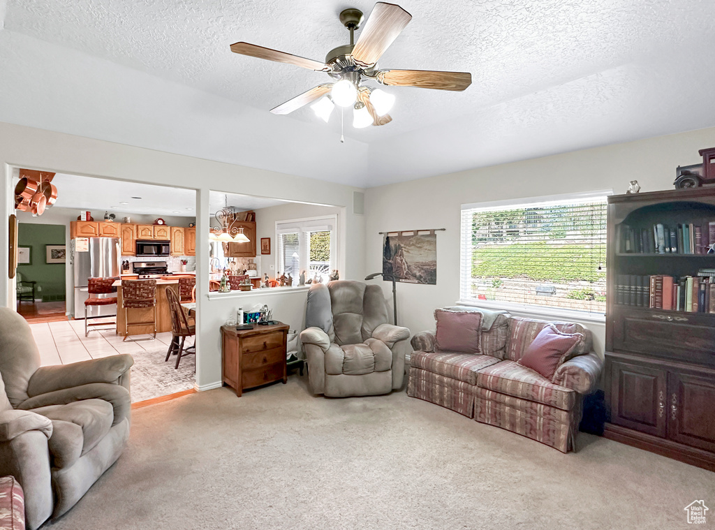 Carpeted living room featuring a textured ceiling, ceiling fan with notable chandelier, and plenty of natural light