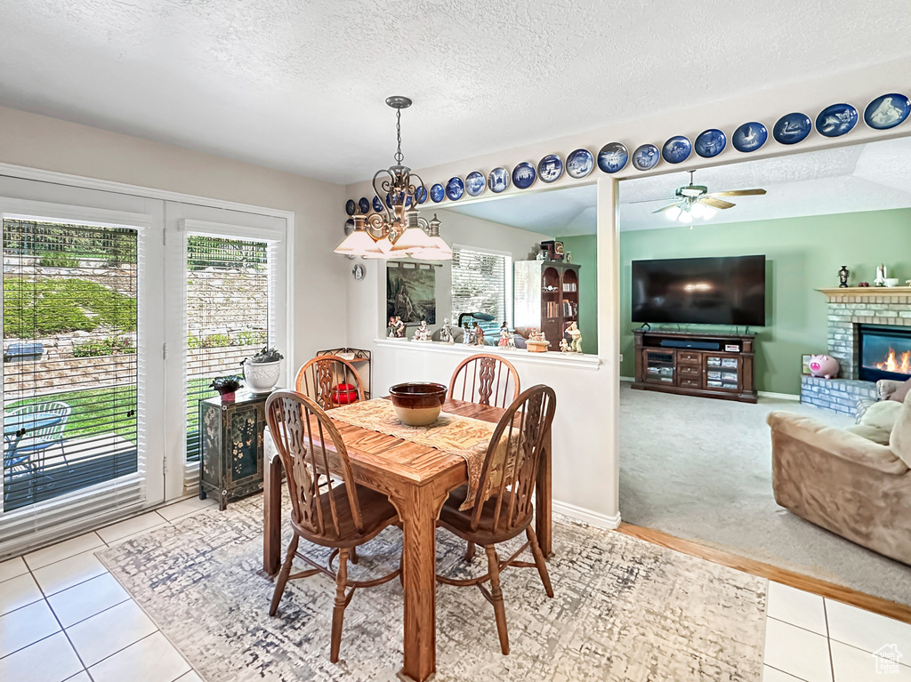 Tiled dining room with a brick fireplace, a textured ceiling, and ceiling fan with notable chandelier