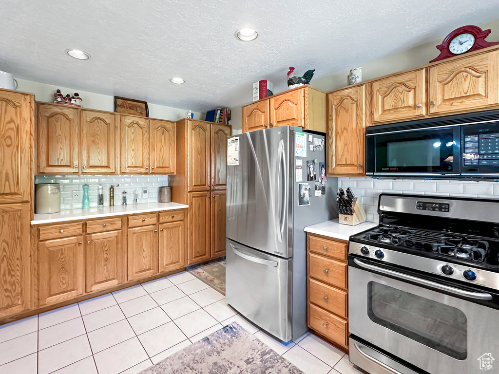 Kitchen with a textured ceiling, backsplash, light tile patterned floors, and stainless steel appliances