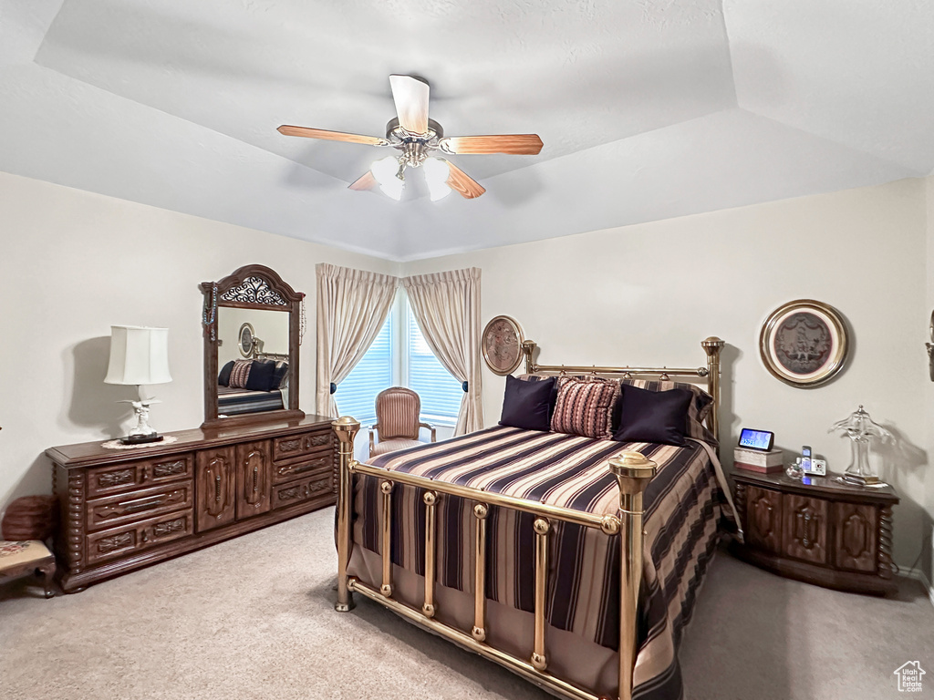 Bedroom with lofted ceiling, a tray ceiling, ceiling fan, and light colored carpet