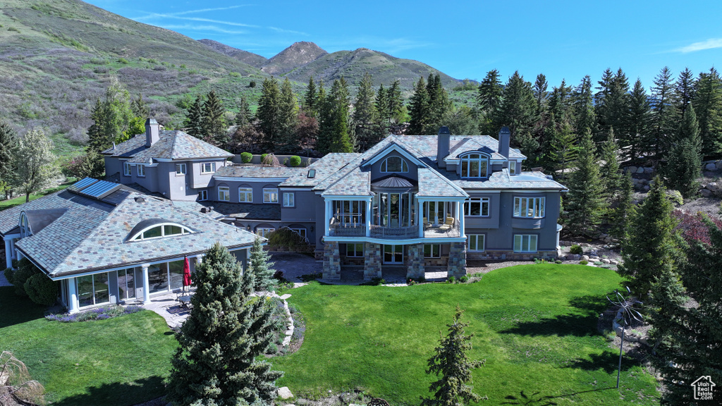 Rear view of house featuring a chimney, a balcony, a lawn, stone siding, and a mountain view
