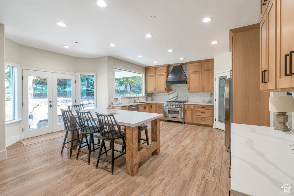 Kitchen featuring custom exhaust hood, french doors, light hardwood / wood-style flooring, appliances with stainless steel finishes, and a breakfast bar