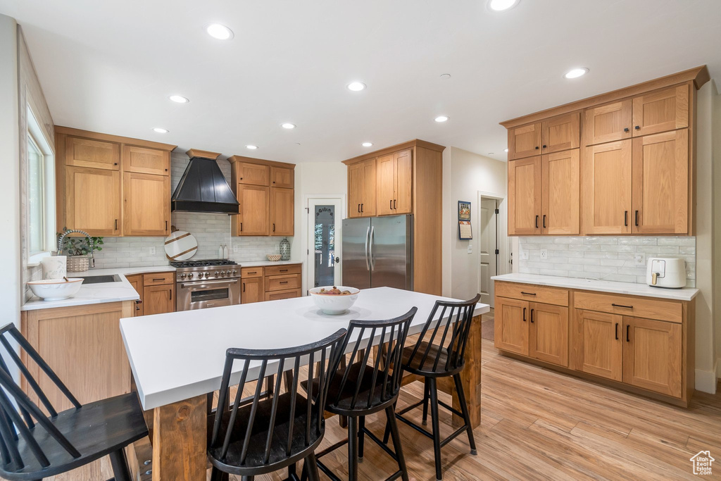 Kitchen featuring custom range hood, decorative backsplash, stainless steel appliances, a kitchen bar, and light hardwood / wood-style flooring