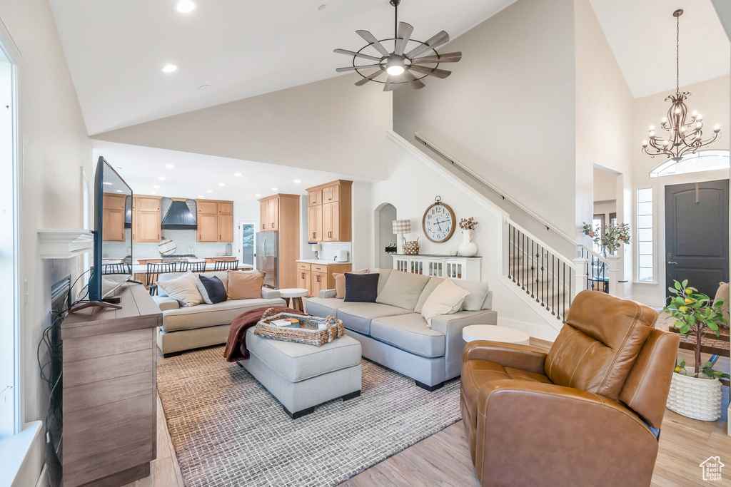 Living room with high vaulted ceiling, light hardwood / wood-style floors, ceiling fan with notable chandelier, and a healthy amount of sunlight