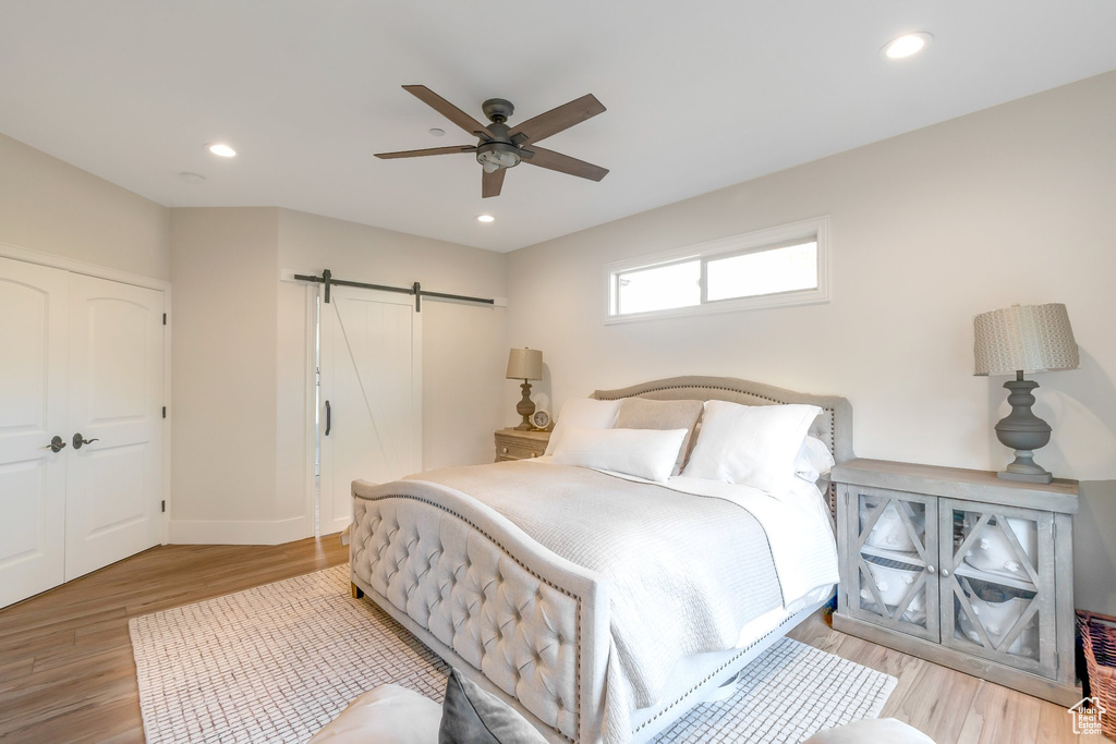 Bedroom with light wood-type flooring, ceiling fan, and a barn door