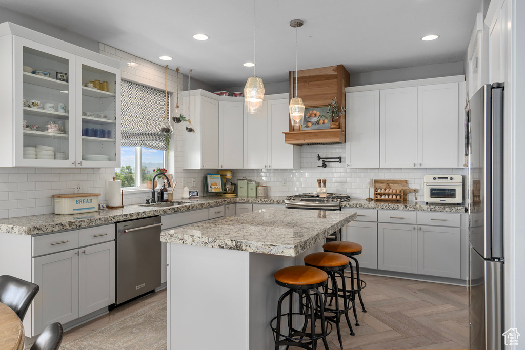 Kitchen featuring appliances with stainless steel finishes, white cabinetry, a kitchen island, pendant lighting, and light parquet floors