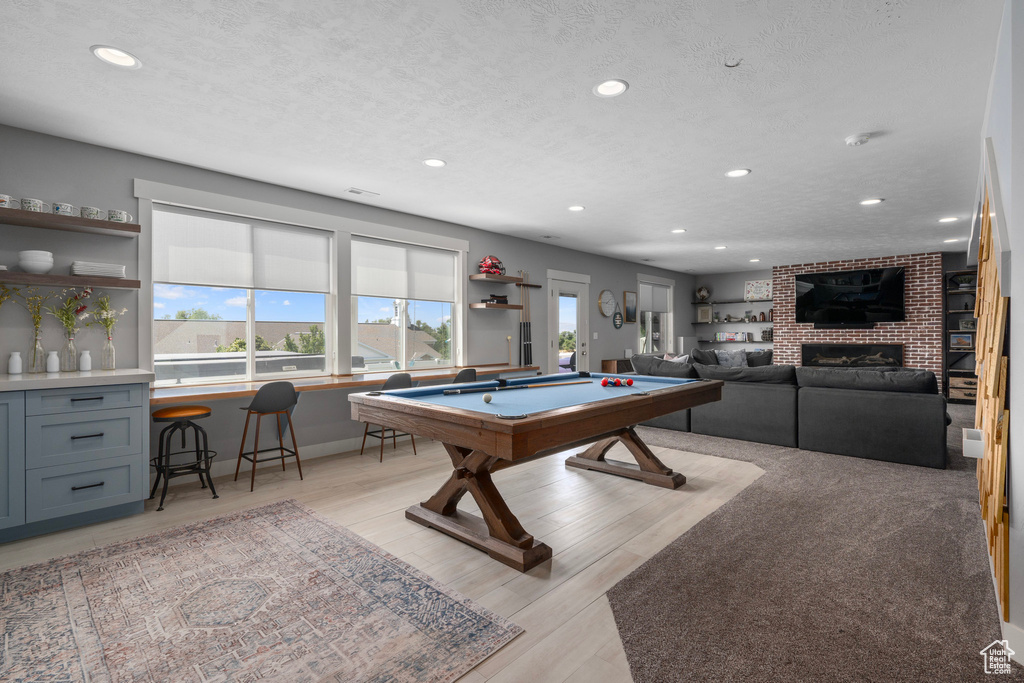 Recreation room featuring a textured ceiling, light hardwood / wood-style flooring, billiards, and a brick fireplace