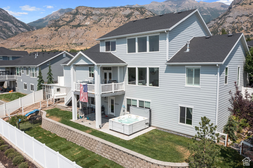 Rear view of house with a lawn, a patio, a mountain view, and a hot tub