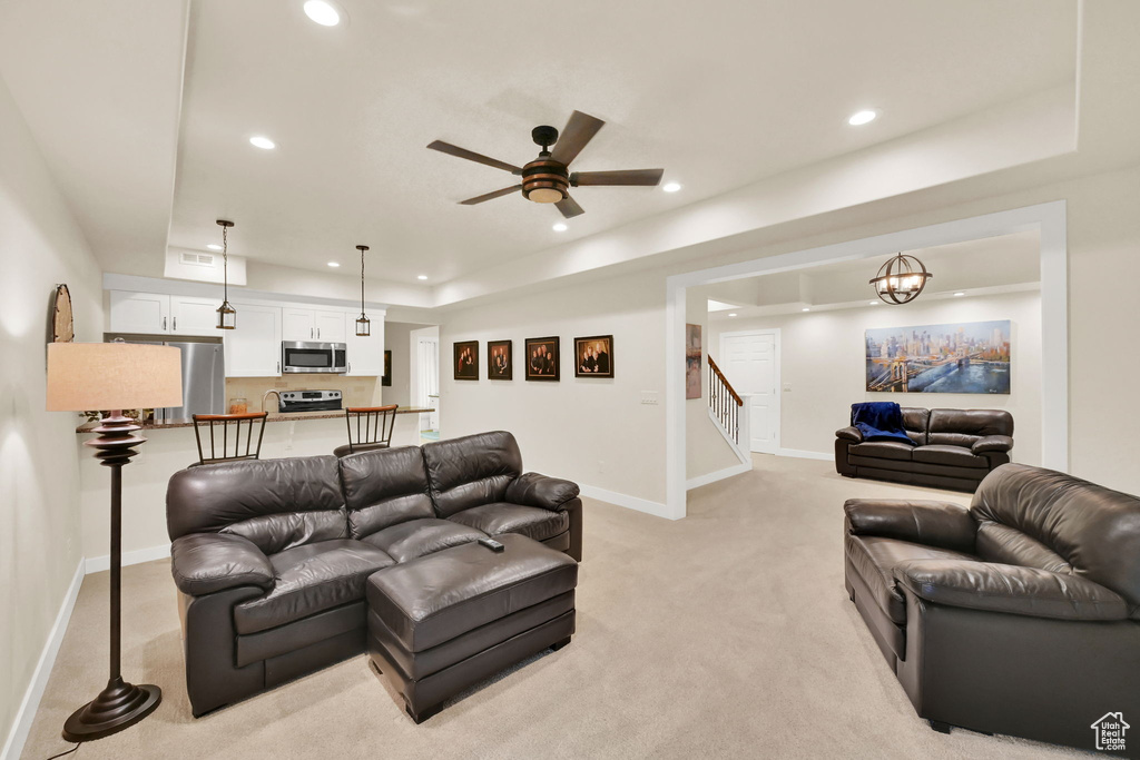 Carpeted living room with ceiling fan with notable chandelier and a tray ceiling