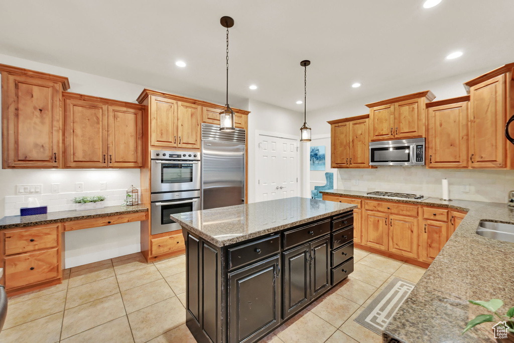 Kitchen with light stone countertops, stainless steel appliances, hanging light fixtures, and a kitchen island