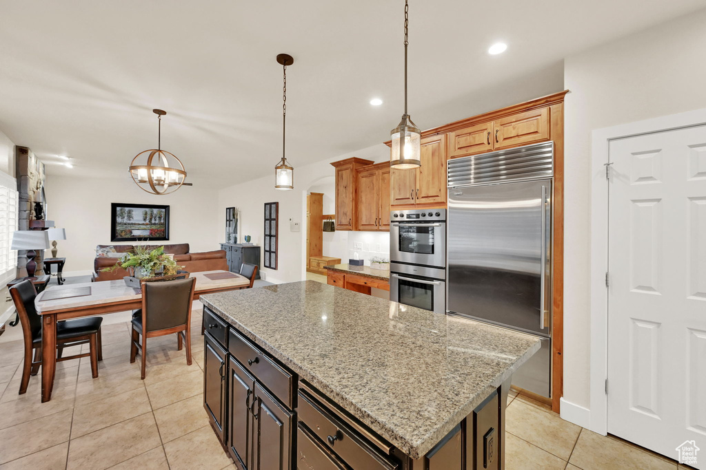 Kitchen with light stone counters, appliances with stainless steel finishes, hanging light fixtures, and a kitchen island