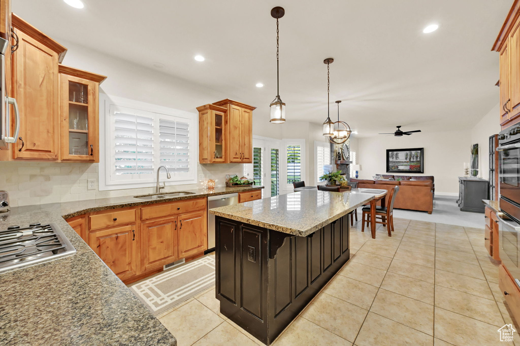 Kitchen featuring ceiling fan with notable chandelier, a kitchen bar, a kitchen island, appliances with stainless steel finishes, and decorative light fixtures