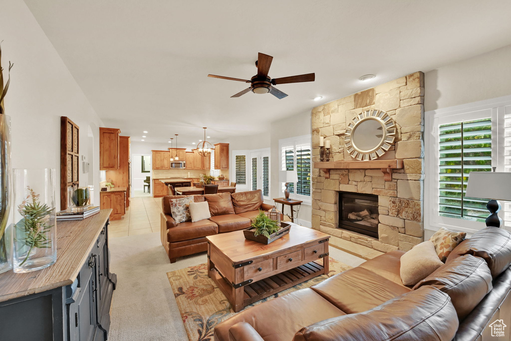 Living room with ceiling fan with notable chandelier, a fireplace, light tile patterned flooring, and a wealth of natural light