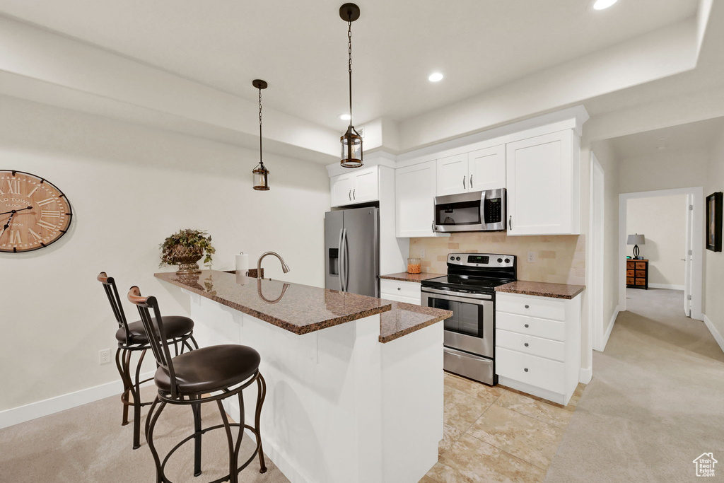 Kitchen with decorative light fixtures, white cabinetry, appliances with stainless steel finishes, light colored carpet, and decorative backsplash