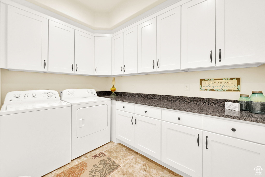 Laundry area featuring separate washer and dryer, light tile patterned floors, and cabinets