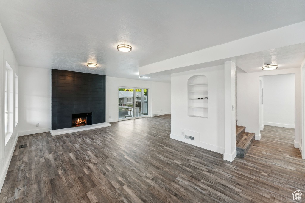 Unfurnished living room with built in shelves, a textured ceiling, a fireplace, and dark wood-type flooring