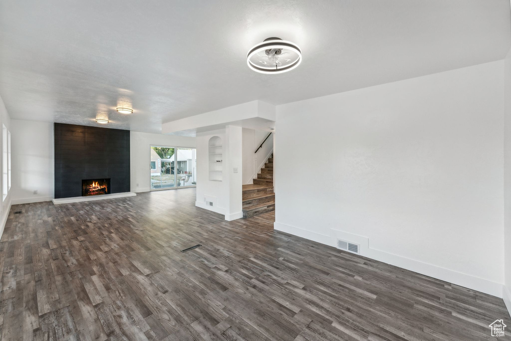 Unfurnished living room featuring dark hardwood / wood-style floors and a large fireplace