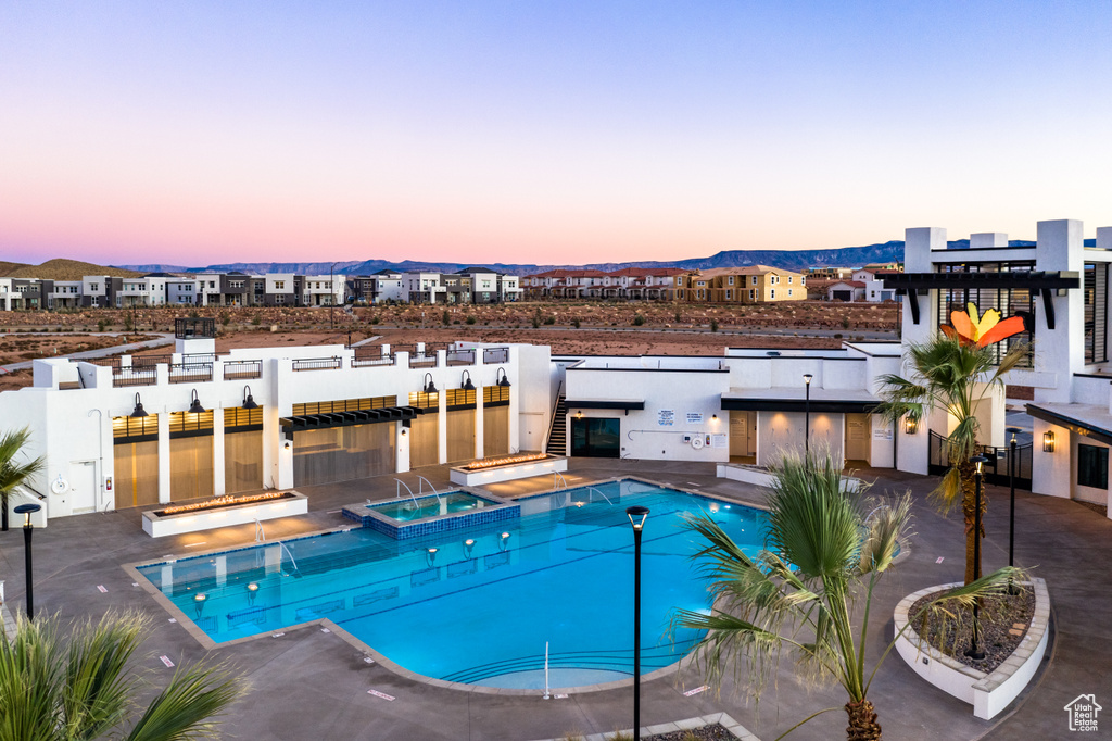 Pool at dusk with a mountain view, a patio, and a hot tub