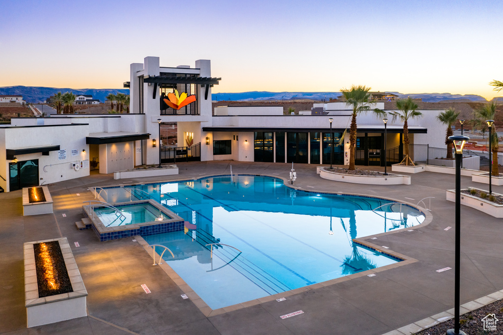 Pool at dusk featuring a patio, a community hot tub, a mountain view, and a fire pit