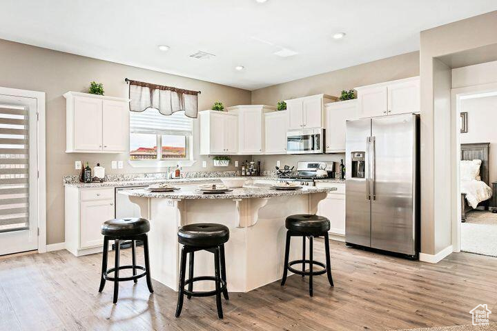 Kitchen with light wood-type flooring, white cabinetry, appliances with stainless steel finishes, and a center island