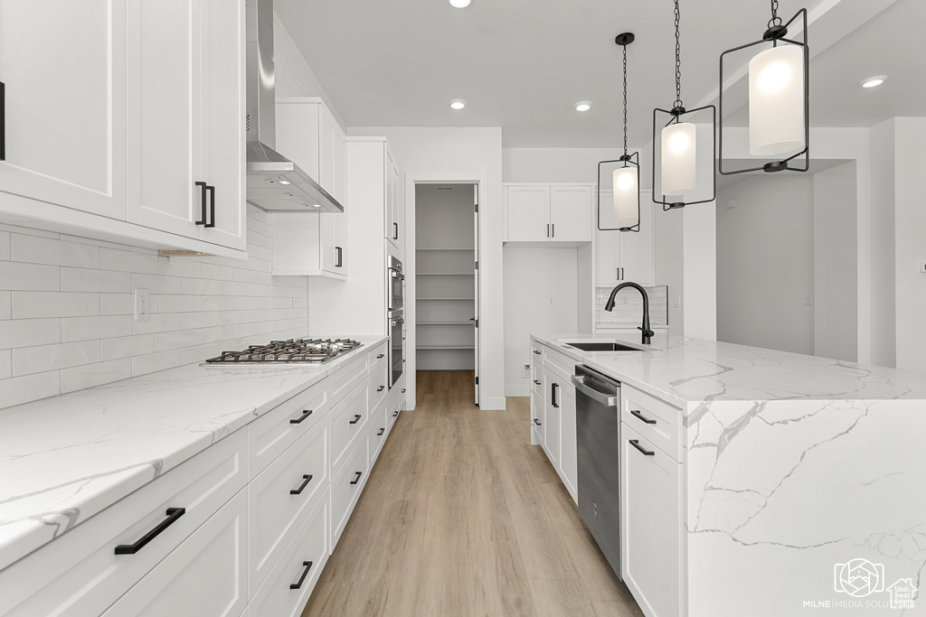 Kitchen featuring wall chimney range hood, white cabinets, hanging light fixtures, stainless steel appliances, and sink