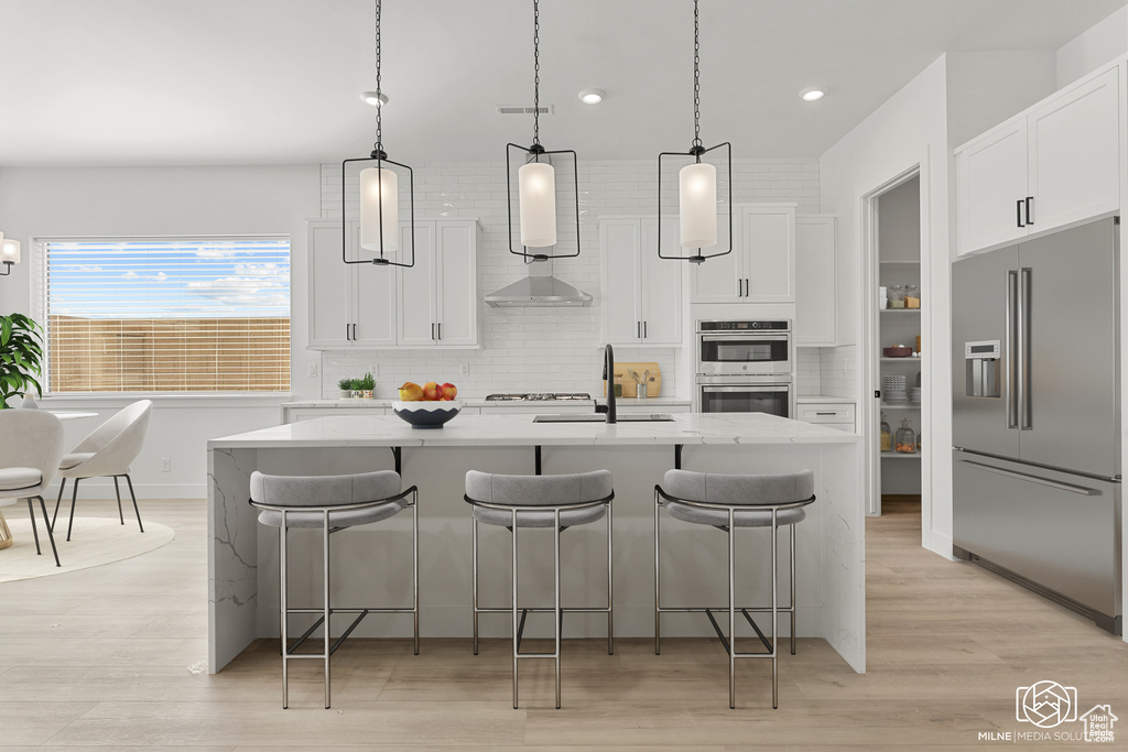 Kitchen featuring appliances with stainless steel finishes, decorative light fixtures, a kitchen island with sink, and white cabinets