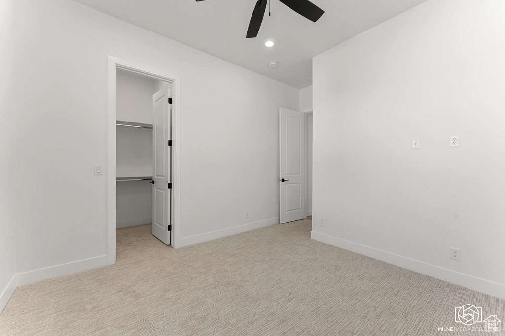 Unfurnished bedroom with a spacious closet, ceiling fan, a closet, and light colored carpet