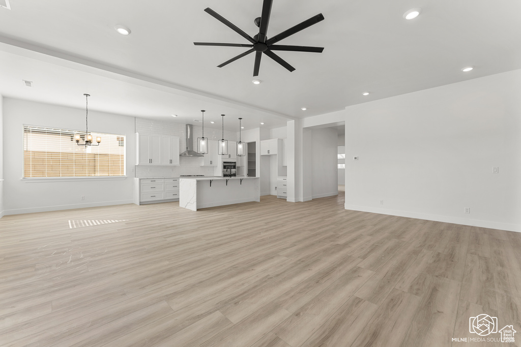 Unfurnished living room featuring light wood-type flooring and ceiling fan with notable chandelier