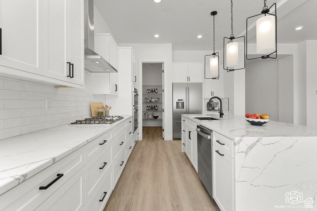 Kitchen featuring wall chimney range hood, appliances with stainless steel finishes, white cabinetry, pendant lighting, and sink